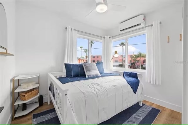 bedroom with wood-type flooring, a wall unit AC, and ceiling fan