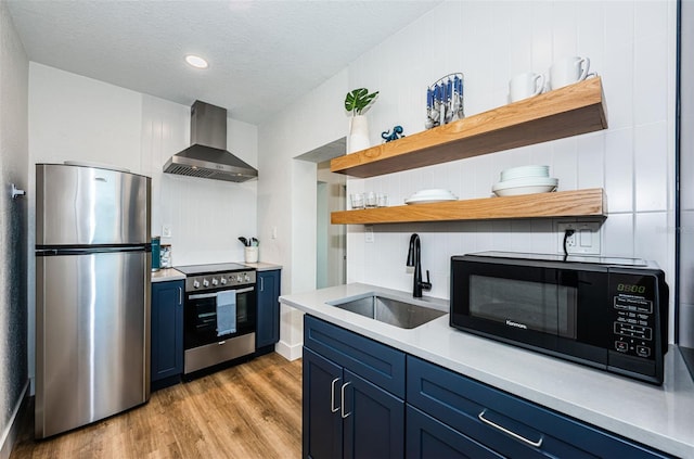 kitchen with stainless steel appliances, sink, wall chimney range hood, and blue cabinetry