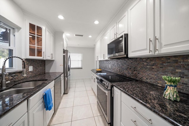 kitchen featuring sink, light tile patterned floors, dark stone countertops, stainless steel appliances, and white cabinets