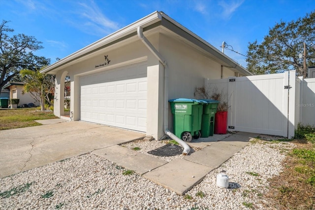 exterior space with stucco siding, a gate, fence, concrete driveway, and a garage