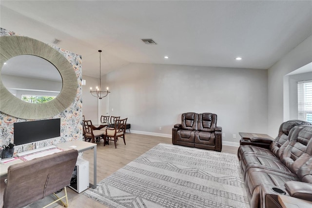 living room with vaulted ceiling, an inviting chandelier, and light hardwood / wood-style floors