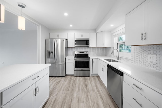 kitchen with sink, decorative light fixtures, light wood-type flooring, appliances with stainless steel finishes, and white cabinets