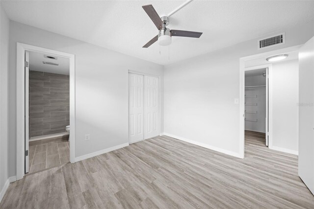 unfurnished bedroom with light hardwood / wood-style flooring, ceiling fan, ensuite bathroom, a textured ceiling, and a closet