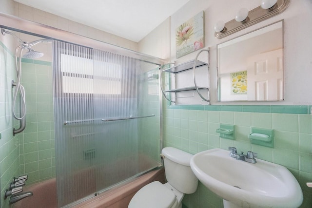 full bathroom with bath / shower combo with glass door, sink, tile walls, and toilet