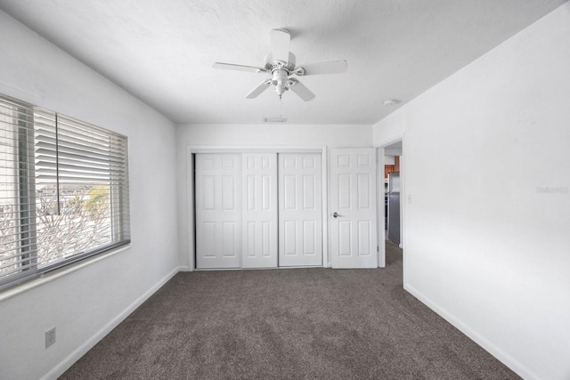 unfurnished bedroom featuring ceiling fan, stainless steel refrigerator, dark carpet, and a closet