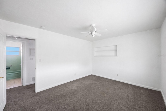 empty room featuring dark colored carpet, ceiling fan, and built in shelves