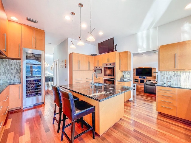 kitchen with a breakfast bar area, double oven, hanging light fixtures, tasteful backsplash, and light wood-type flooring