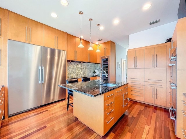 kitchen with sink, stainless steel refrigerator, a breakfast bar, a kitchen island with sink, and decorative light fixtures