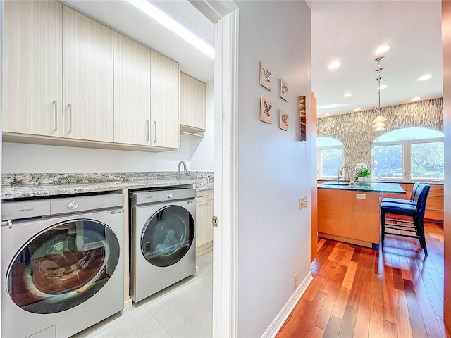 clothes washing area featuring separate washer and dryer, sink, light hardwood / wood-style flooring, and cabinets