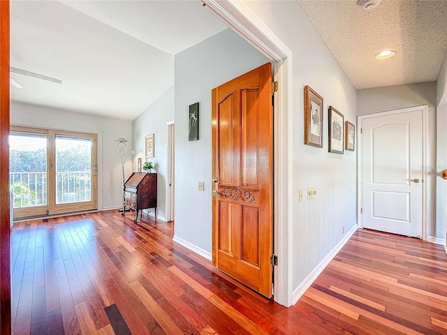 corridor with hardwood / wood-style flooring, vaulted ceiling, and a textured ceiling