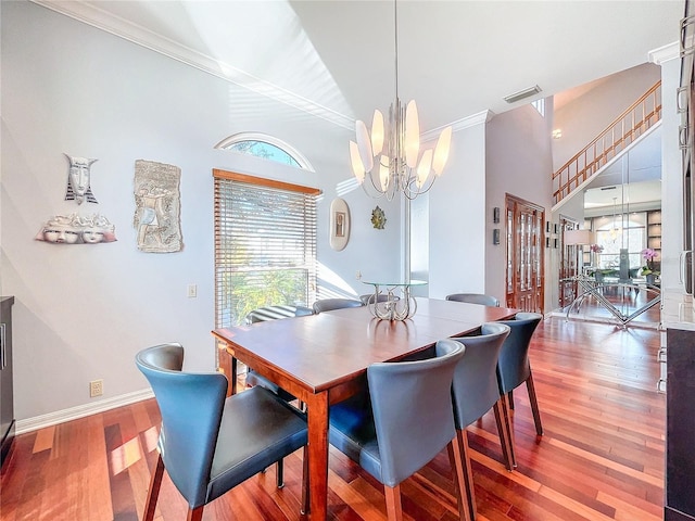 dining area with wood-type flooring, plenty of natural light, crown molding, and an inviting chandelier