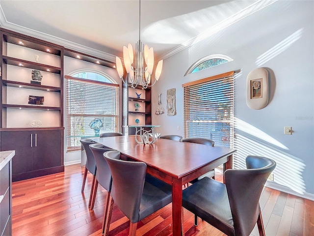 dining area featuring crown molding, built in features, an inviting chandelier, and light hardwood / wood-style flooring