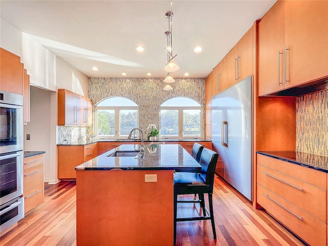 kitchen featuring pendant lighting, sink, appliances with stainless steel finishes, a kitchen island with sink, and backsplash