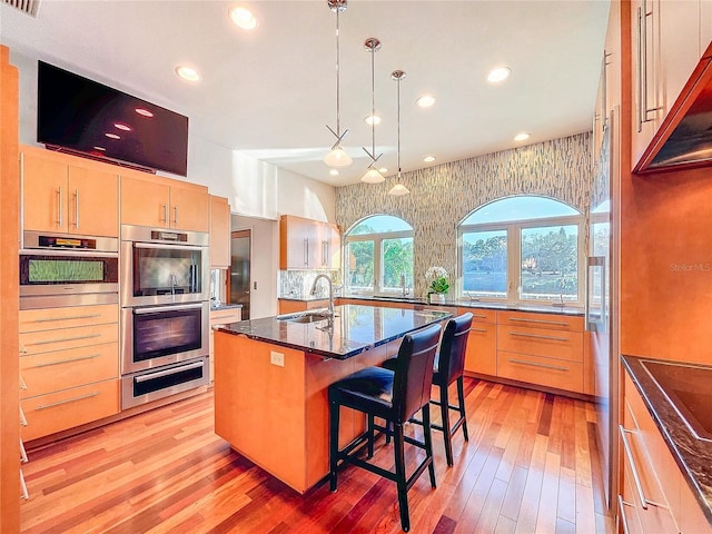 kitchen featuring decorative light fixtures, an island with sink, sink, a kitchen breakfast bar, and stainless steel double oven