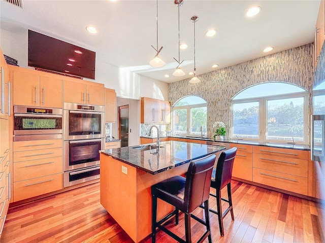 kitchen with sink, a kitchen island with sink, double oven, a kitchen bar, and light brown cabinetry