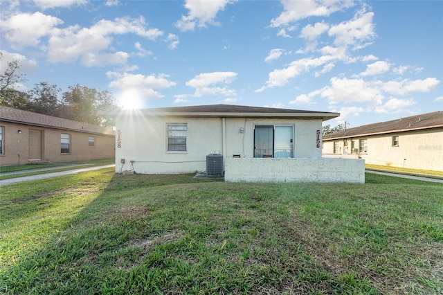 rear view of property featuring a yard, stucco siding, and central air condition unit