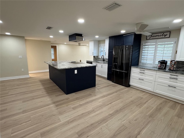 kitchen featuring a kitchen island, black appliances, white cabinets, light hardwood / wood-style floors, and light stone counters