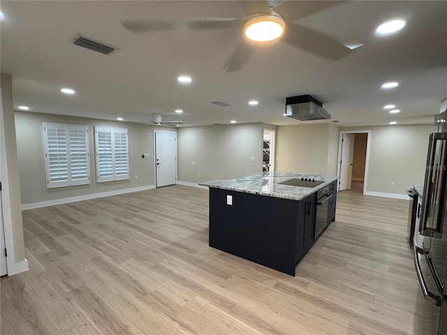 kitchen with ceiling fan, light stone counters, black appliances, an island with sink, and light wood-type flooring