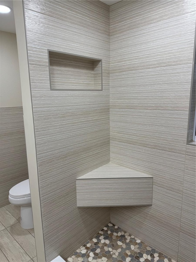 bathroom featuring tile patterned flooring, a tile shower, and toilet