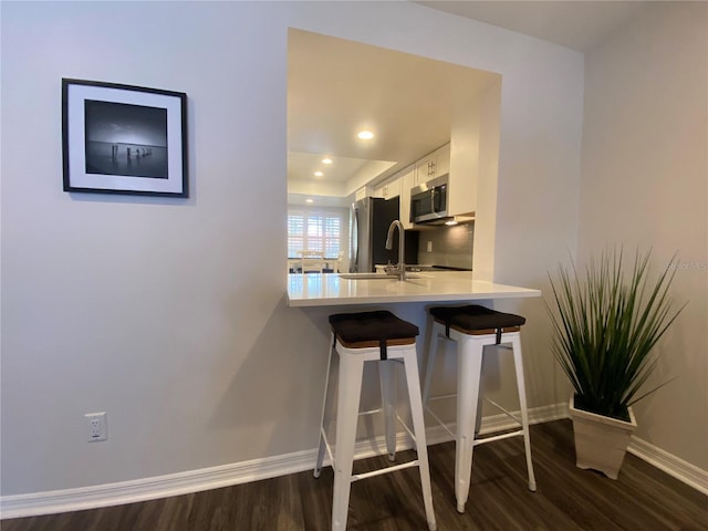 kitchen featuring appliances with stainless steel finishes, dark hardwood / wood-style floors, a breakfast bar area, and white cabinets