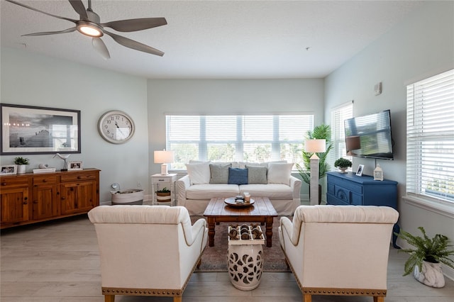 living room with a textured ceiling, ceiling fan, and light wood-type flooring