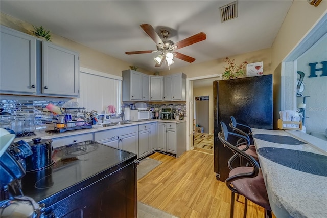 kitchen featuring sink, backsplash, light hardwood / wood-style flooring, and black appliances