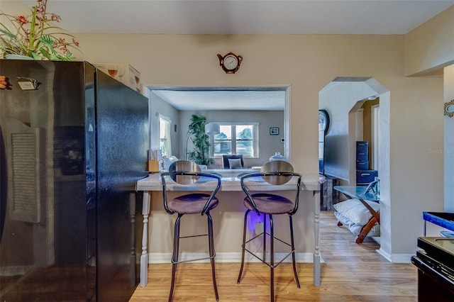 kitchen with black refrigerator, a kitchen breakfast bar, and light hardwood / wood-style flooring