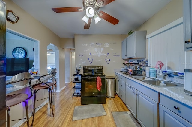 kitchen featuring backsplash, black electric range oven, sink, and light wood-type flooring