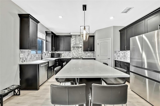 kitchen featuring a kitchen island, decorative light fixtures, sink, stainless steel appliances, and wall chimney range hood