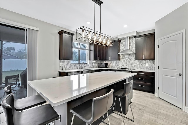 kitchen featuring decorative light fixtures, a kitchen bar, a center island, dark brown cabinets, and wall chimney exhaust hood