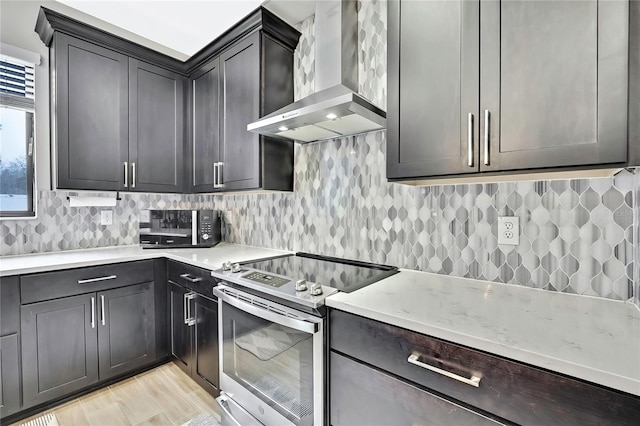 kitchen featuring light stone countertops, stainless steel electric range oven, decorative backsplash, wall chimney exhaust hood, and light wood-type flooring