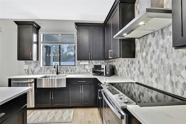 kitchen with sink, light wood-type flooring, stainless steel appliances, decorative backsplash, and wall chimney range hood