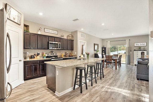 kitchen with an island with sink, a breakfast bar area, dark brown cabinetry, stainless steel appliances, and light hardwood / wood-style flooring