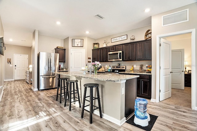 kitchen with stainless steel appliances, a center island with sink, dark brown cabinetry, and light hardwood / wood-style floors