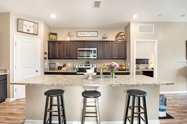 kitchen with dark brown cabinetry, appliances with stainless steel finishes, a kitchen island with sink, and a breakfast bar area