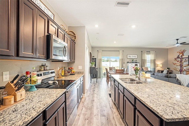 kitchen with appliances with stainless steel finishes, sink, light stone counters, dark brown cabinetry, and light hardwood / wood-style flooring