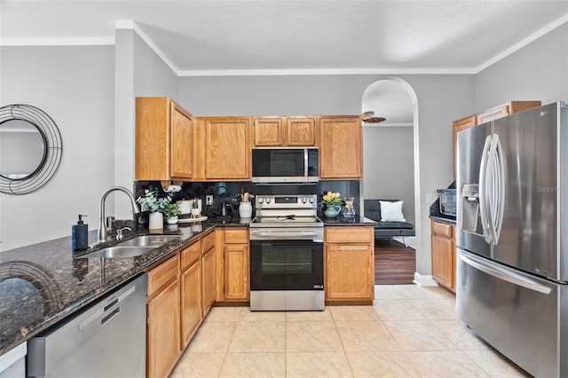 kitchen with dark stone countertops, sink, ornamental molding, and appliances with stainless steel finishes