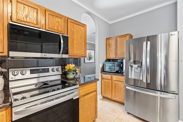 kitchen with appliances with stainless steel finishes, dark stone countertops, backsplash, ornamental molding, and light tile patterned floors