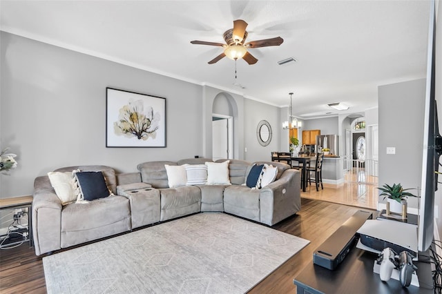 living room featuring dark hardwood / wood-style flooring, ceiling fan with notable chandelier, and ornamental molding