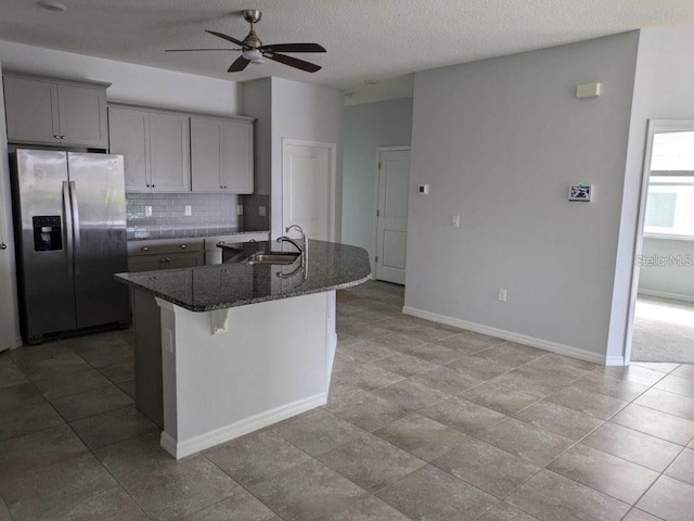 kitchen with a kitchen bar, sink, gray cabinetry, a center island with sink, and stainless steel fridge