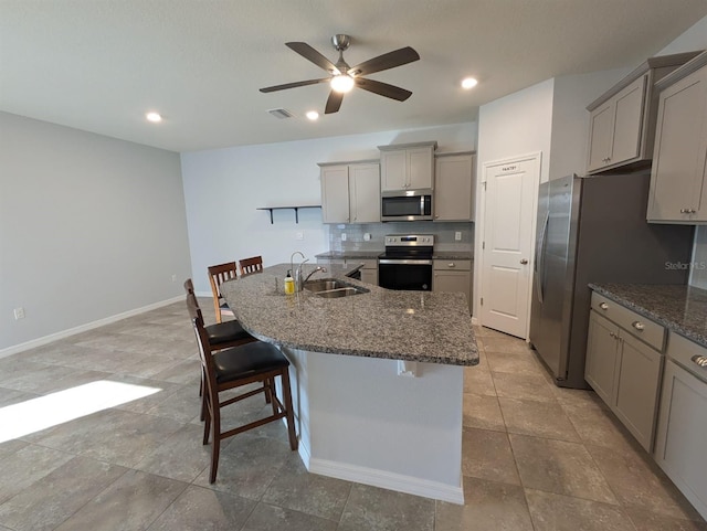 kitchen featuring a kitchen bar, sink, gray cabinetry, an island with sink, and stainless steel appliances