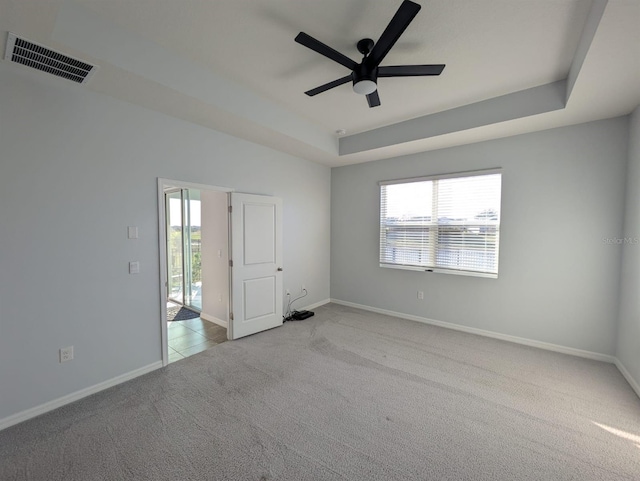 spare room featuring ceiling fan, light colored carpet, and a raised ceiling