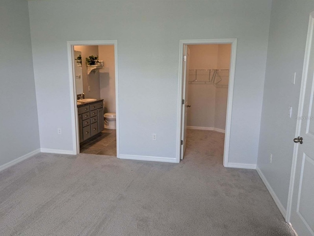 unfurnished bedroom featuring connected bathroom, sink, a spacious closet, light colored carpet, and a closet