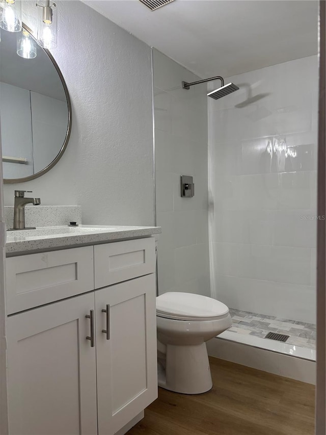 bathroom featuring vanity, hardwood / wood-style floors, toilet, and a tile shower