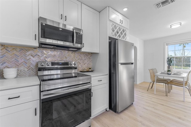 kitchen featuring tasteful backsplash, appliances with stainless steel finishes, light hardwood / wood-style floors, and white cabinets