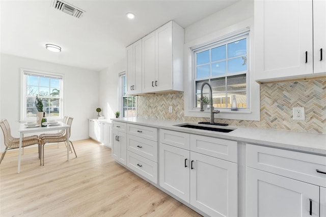 kitchen featuring sink, white cabinetry, light wood-type flooring, light stone countertops, and decorative backsplash