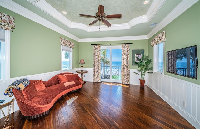 living area with a raised ceiling, wood-type flooring, ornamental molding, and a textured ceiling