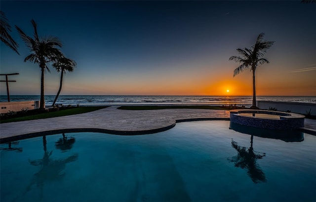 pool at dusk featuring an in ground hot tub and a water view