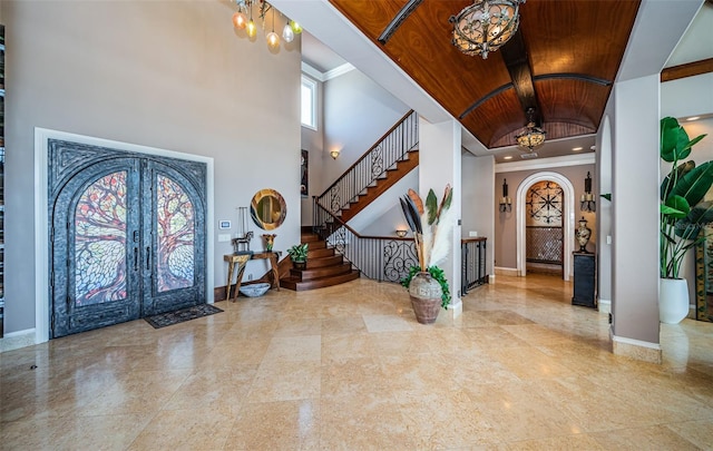 foyer with a towering ceiling, ornamental molding, wooden ceiling, and french doors