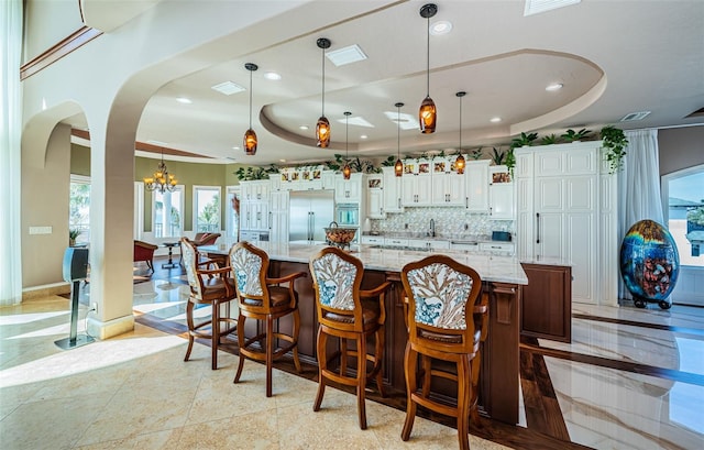 bar featuring stainless steel built in refrigerator, decorative light fixtures, and a tray ceiling